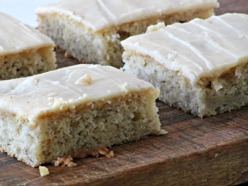 banana bars with browned butter frosting cut and served on a wood cutting board.