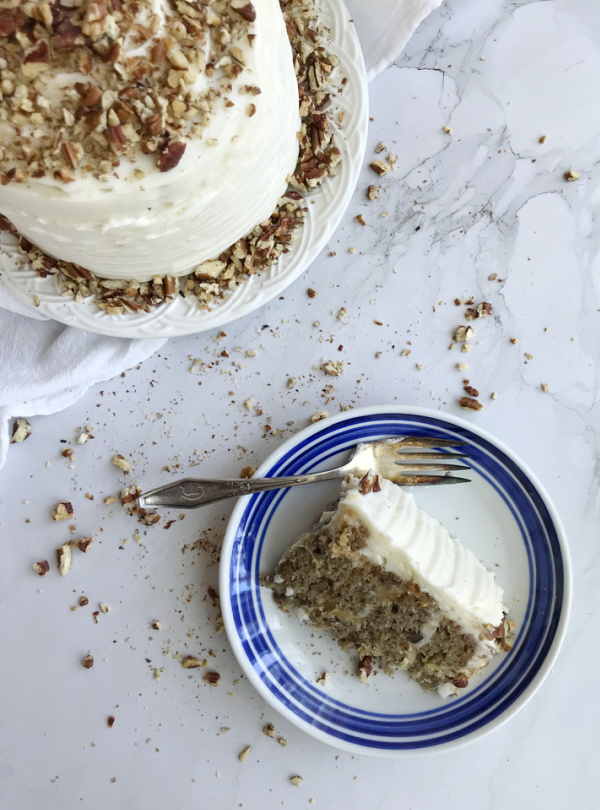 Hummingbird Cake on a cake stand with a piece on a blue and whit plate next to it.