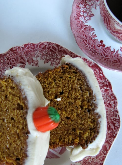 Pumpkin loaf with cream cheese frosting on a red and white transfer ware plate with a cup of tea. 