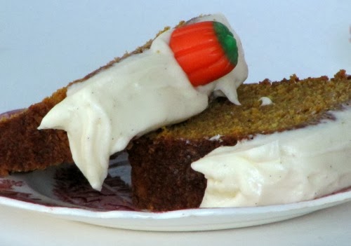 Two pieces of pumpkin loaf with cream cheese frosting and an orange pumpkin candy on top.