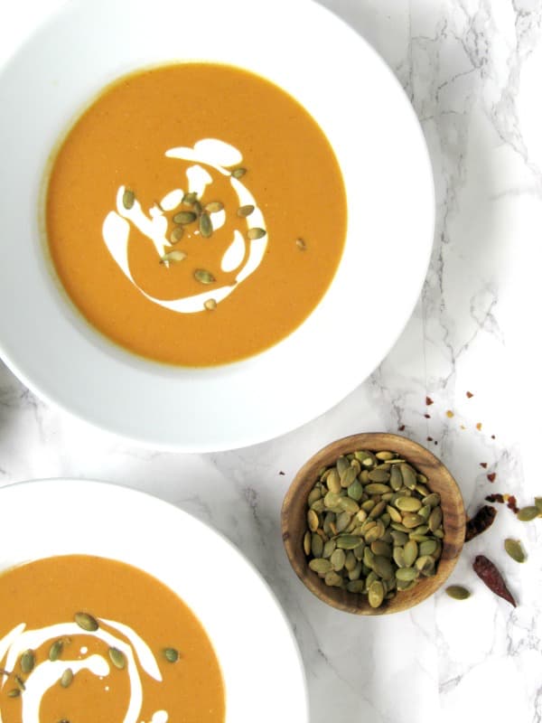 creamy pumpkin ginger soup in a white bowl with toasted pumpkin seeds