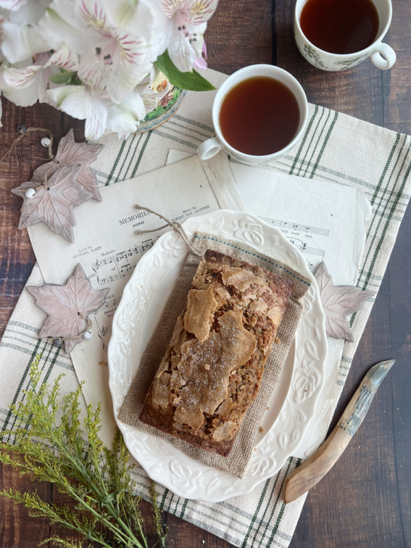 pumpkin zucchini bread flatlay on a green and white check tea towel with a cup of tea and a bone handled knife. 