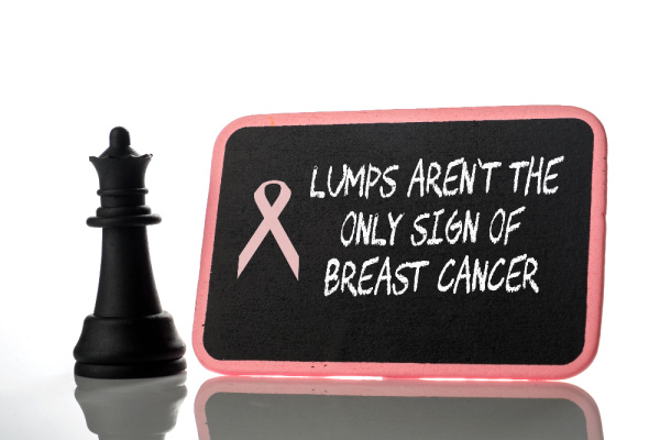 a black chess piece with a black chalkboard rimmed in pink that says lumps are not the only sign of breast cancer