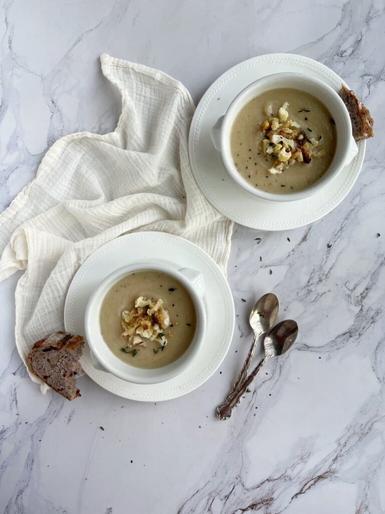 caramelized onion and cauliflower soup in two white bowls with bread.