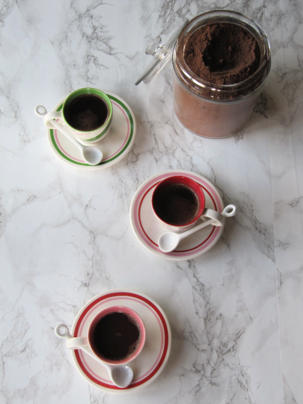 2 cups of hot chocolate and a glass canister with coco mix