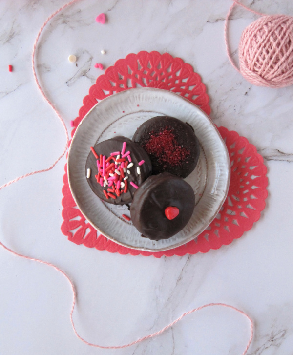 Chocolate covered Oreo cookies on a heart shaped plate sitting on a red doily 