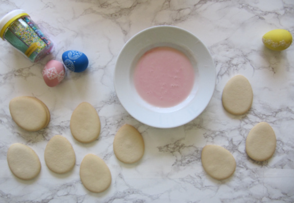 Sugar cookies egg shaped and a bowl of pastel pink frosting