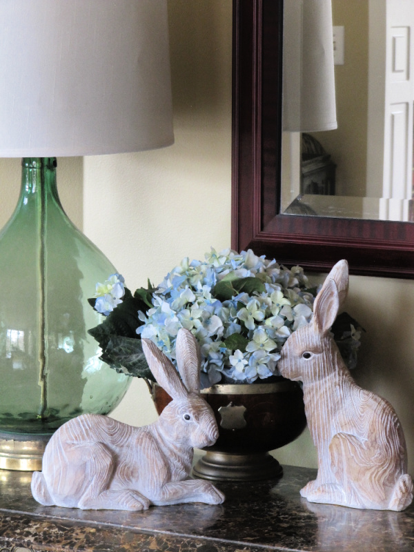 two wood easter bunnies a bowl of hydrangeas and a Demi John lamp on a marble table