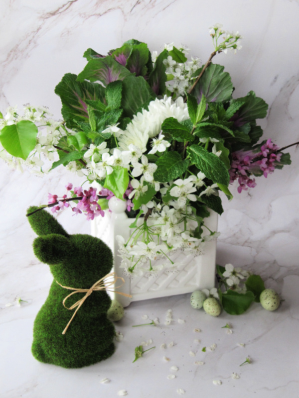 Flower arrangement in a white porcelain planter with a green moss bunny next to it