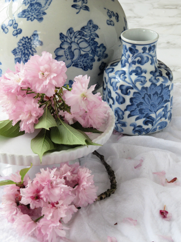 pink cherry blossoms on a white cake plate with blue and white chinoiserie vases pinecones and acorns blog