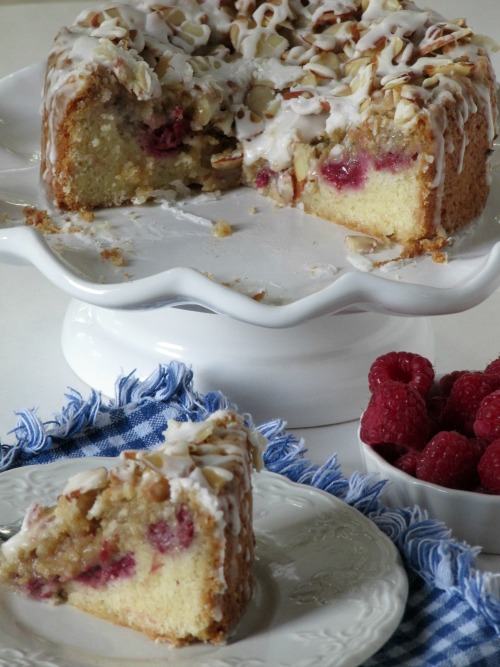  5 mothers day gift idea raspberry almond coffeecake on a white cake plate and a piece on a small white plate with a bowl of raspberries. 