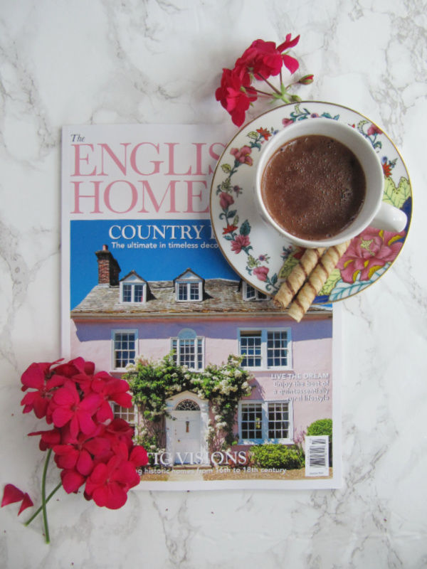 The English Home Magazine with a cup of hot chocolate and a few fuchsia colored geraniums on a white marble background pinecones and acorns blog