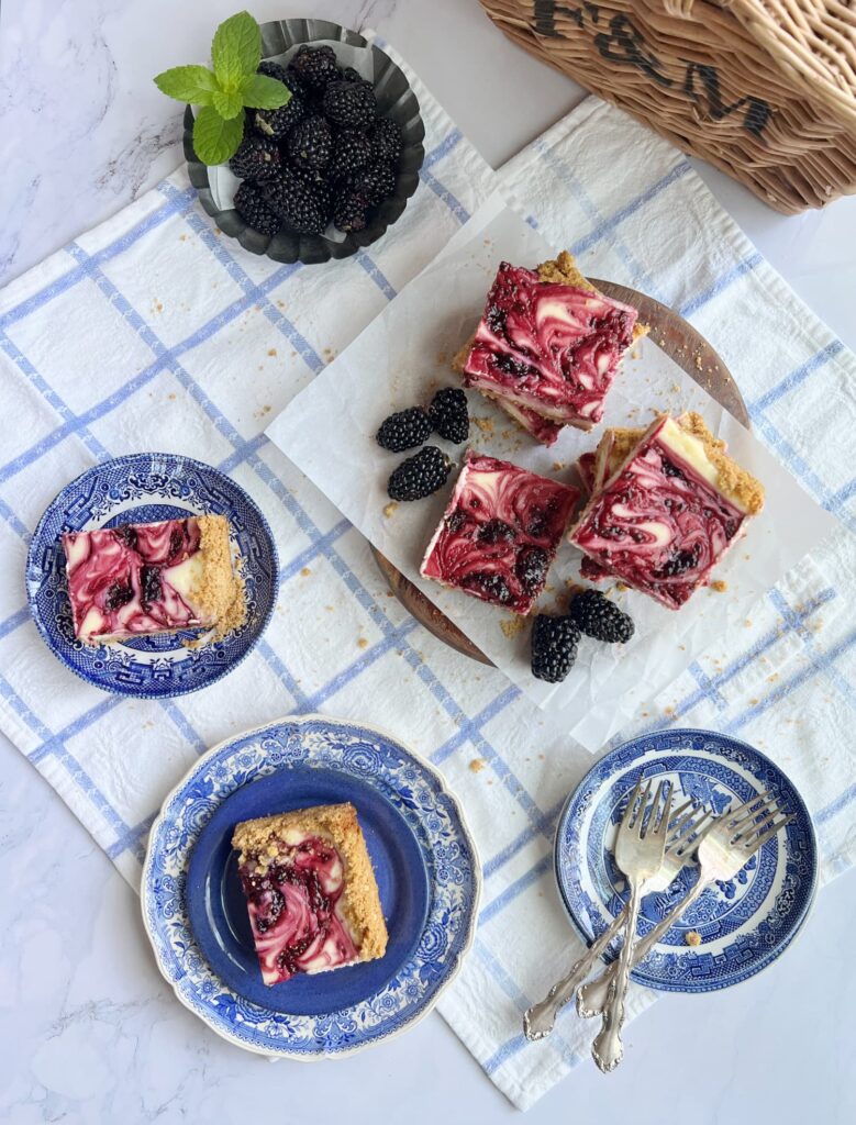 blackberry cheesecake bars flatlay with a picnic basket and blackberries on a plate