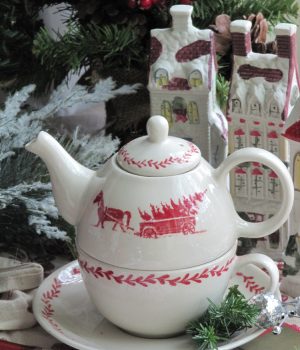 Red and White Williamsburg Teapot sitting in front of two porcelain houses and christmas foliage