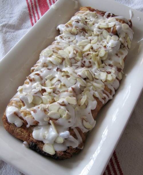 a white rectangular platter with a Danish pastry braid with frosting and slivered almonds