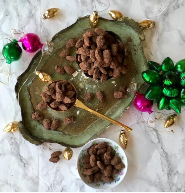 Chocolate almonds dragees in small bowls sitting on a vintage Florentine green tray with bright green and pink christmas ornaments as accents
