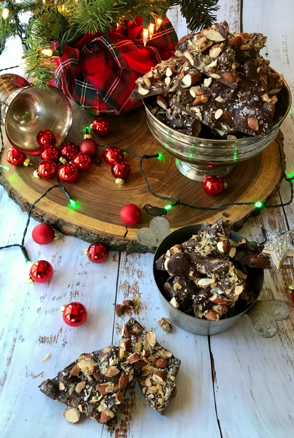 caramelized almond dark chocolate bark in a silver bowl with red Christmas ornaments scattered around
