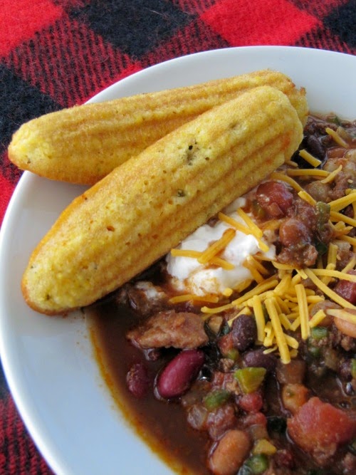 red and black wool table cloth with a white bowl of chili and two cornbread sticks