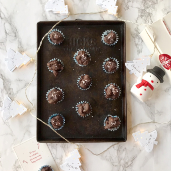 chocolate covered cashews pistachios and dark cherries on a vintage cookie pan with White Christmas tree lights and a small snowman