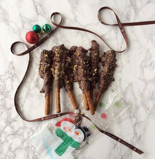 chocolate covered pretzels with nuts on a marble slab with a brown ribbon and christmas ornaments in red and green and cellophane bags with snowmen