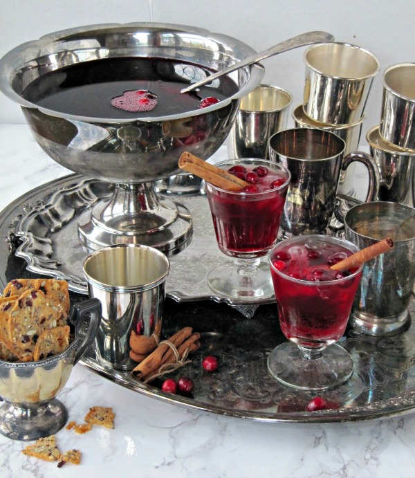 cranberry-bourbon-punch- in a silver punch bowl with silver cups and clear glasses with cranberries and cinnamon sticks