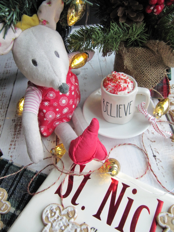 flatly of St.Nicholas books and a small bonus with a cup of hot chocolate on a green plaid background with gingerbread men and christmas lights.
