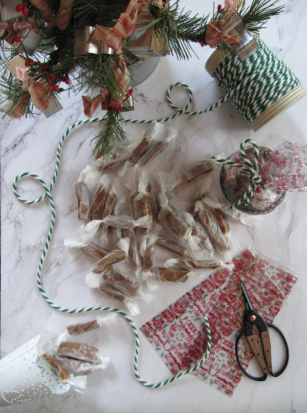 flatly on white marble with a christmas tree green and white twine cellophane bags sissors and homemade caramels wrapped in waxed paper