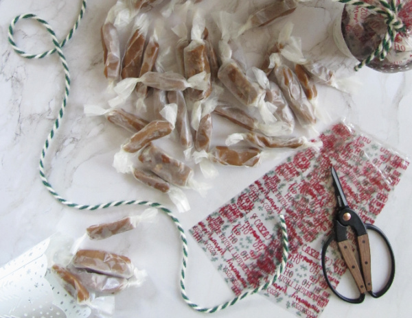 flatly on white marble with a christmas tree green and white twine cellophane bags sissors and homemade caramels wrapped in waxed paper
