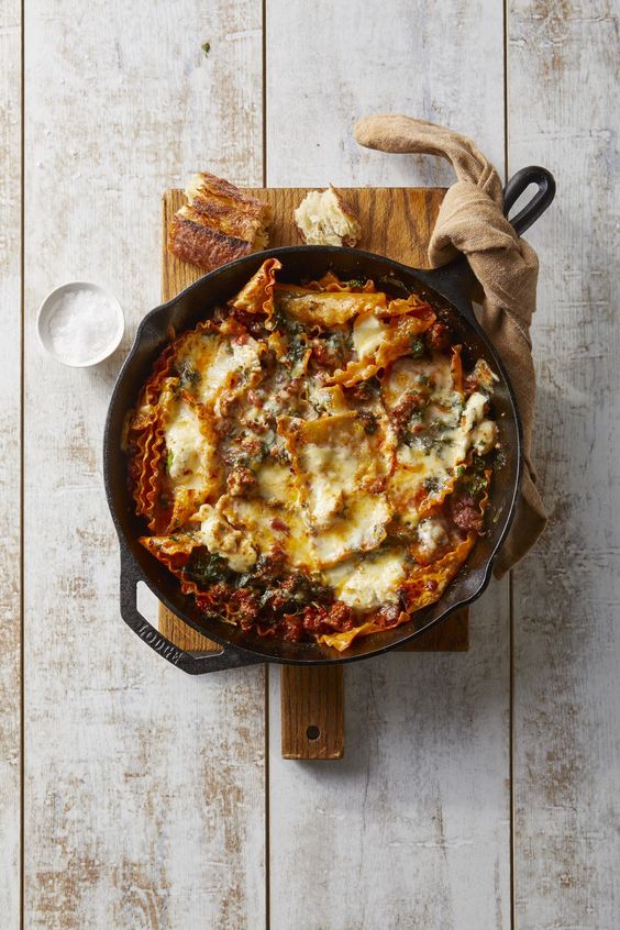 cheese and sausage lasagna in a cast iron skillet sitting on a wood handled cutting board 