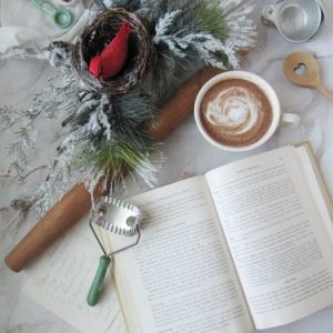 Flatlay with vintage cookbook, handwritten recipe, cup of hot chocolate, evergreen and a nest with a cardinal and various vintage cooking tools