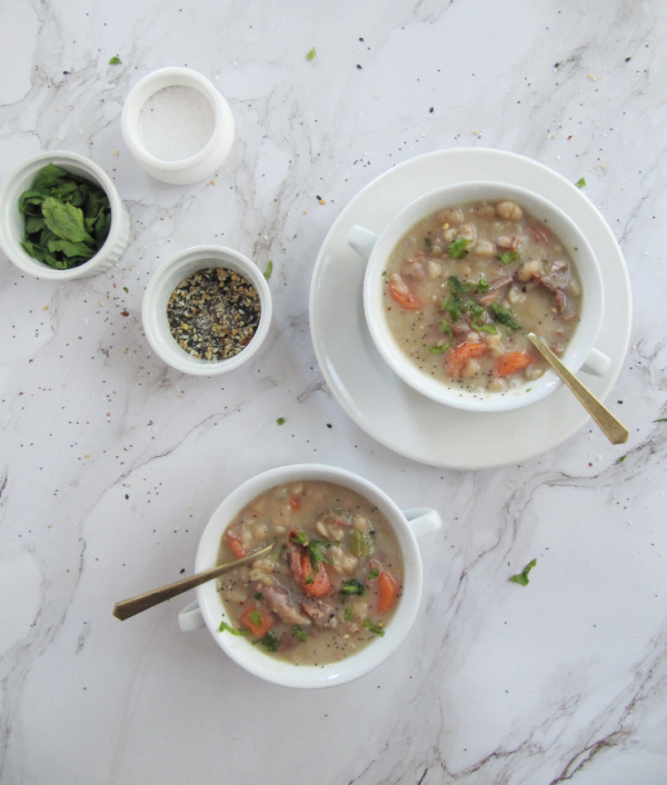 ham and bean soup in white bowls with salt pepper and green herbs in small bowls
