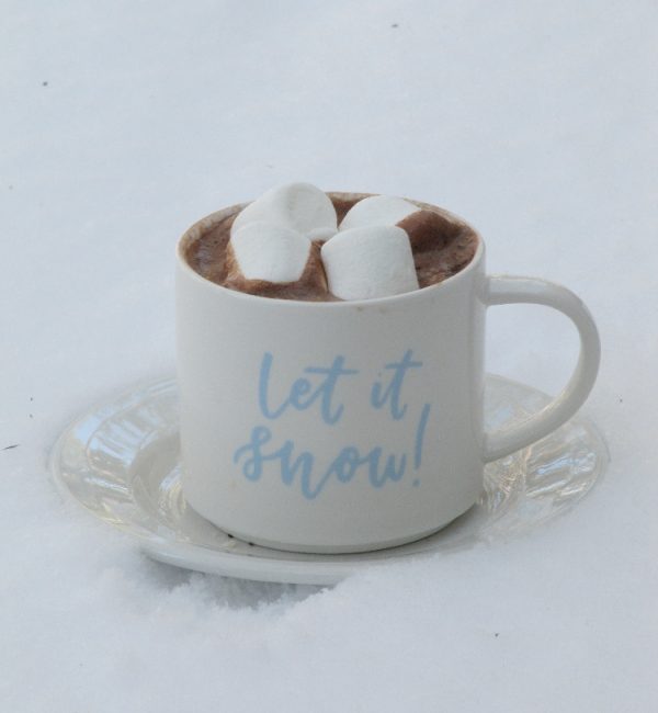 hot chocolate and marshmallows in a let it snow mug on a snow topped table