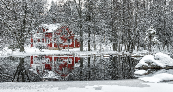 red house in the winter woods with a small pond