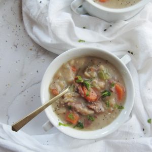 two white bowls with handles filled with ham and bean soup with carrots on has a gold spoon
