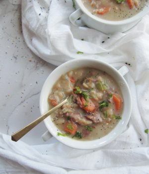 two white bowls with handles filled with ham and bean soup with carrots on has a gold spoon
