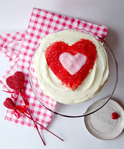 chocolate-cake-buttercream-frosting with a Fred and pick sprinkle heart on a pink gingham napkin with two read hearts on sticks next to it