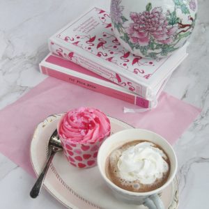 pink cupcake with a cup of hot chocolate and two books
