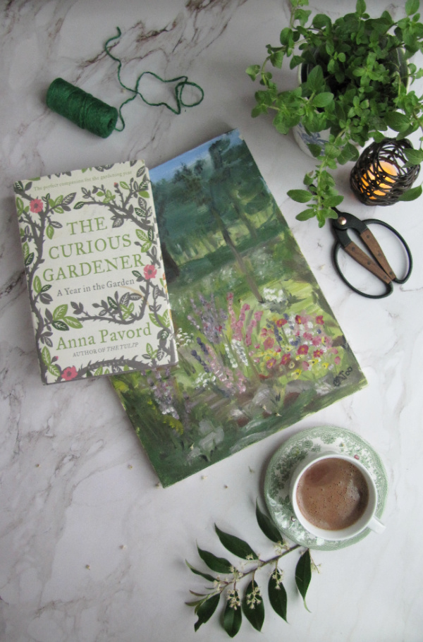 flatly with books herbs scissors hot chocolate and a painting of a garden