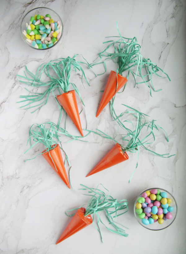 surprise easter carrots on a marble table with two bowls of colorful pastel candy. 