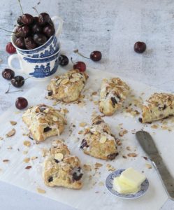 Cherry almond scorns and a blue and white cup of fresh cherries. 