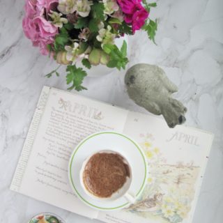 flatlay book open to April flowers concrete bird chocolate and cookies