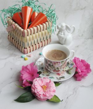 wicker basket with orange paper carrots and a floral cup with hot chocolate and camellia flowers