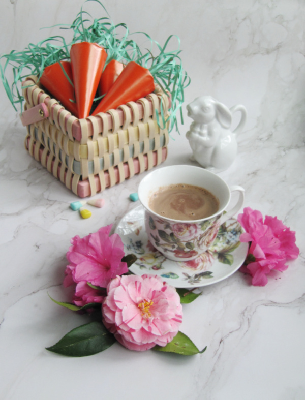 wicker basket with orange paper carrots and a floral cup with hot chocolate and camellia flowers