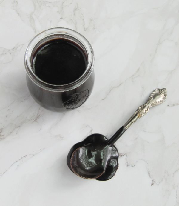 homemade hot fudge sauce in a jar with a spoon full next to it.