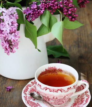lilacs in white pitcher and red transfer ware cup filled with tea