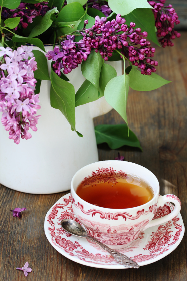lilacs in white pitcher and red transfer ware cup filled with tea