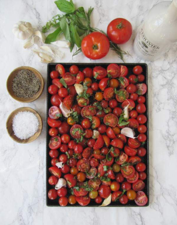 Roasted-tomatoes on a pan with a bowl of salt and pepper on the side