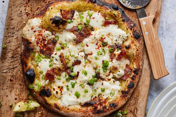 friday favorites bacon goat cheese and leek pizza on a wood cutting board with a pizza cutter