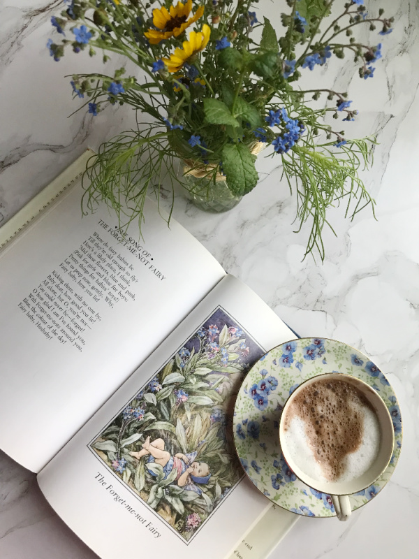 friday favorites cup oc hot chocolate on a flowered saucer jar of wildflowers and a flower fairies book