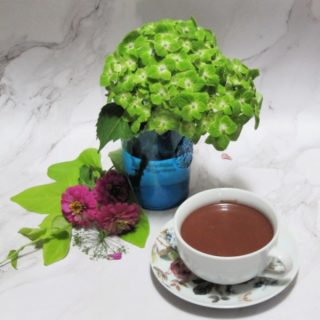 green hydrangea in a blue glass with sweet potato vine pink zinnias and cup of hot chocolate